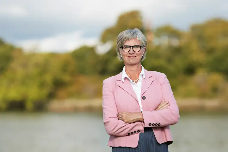 Bettina Lundgren i lyserød blazer, hvid skjorte, smil uden tænder og armene over kors. Billedet er beskåret ved hoften.